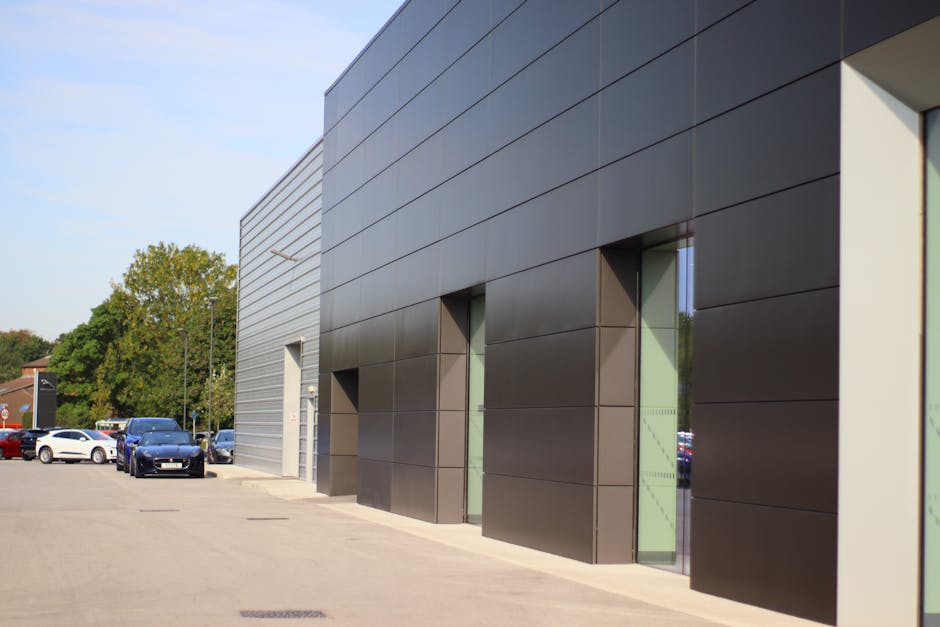 Exterior view of a modern commercial building at Harold Park Industrial Estate with dark grey panelled walls and narrow vertical glass windows. Several cardboard boxes and packing materials are placed
